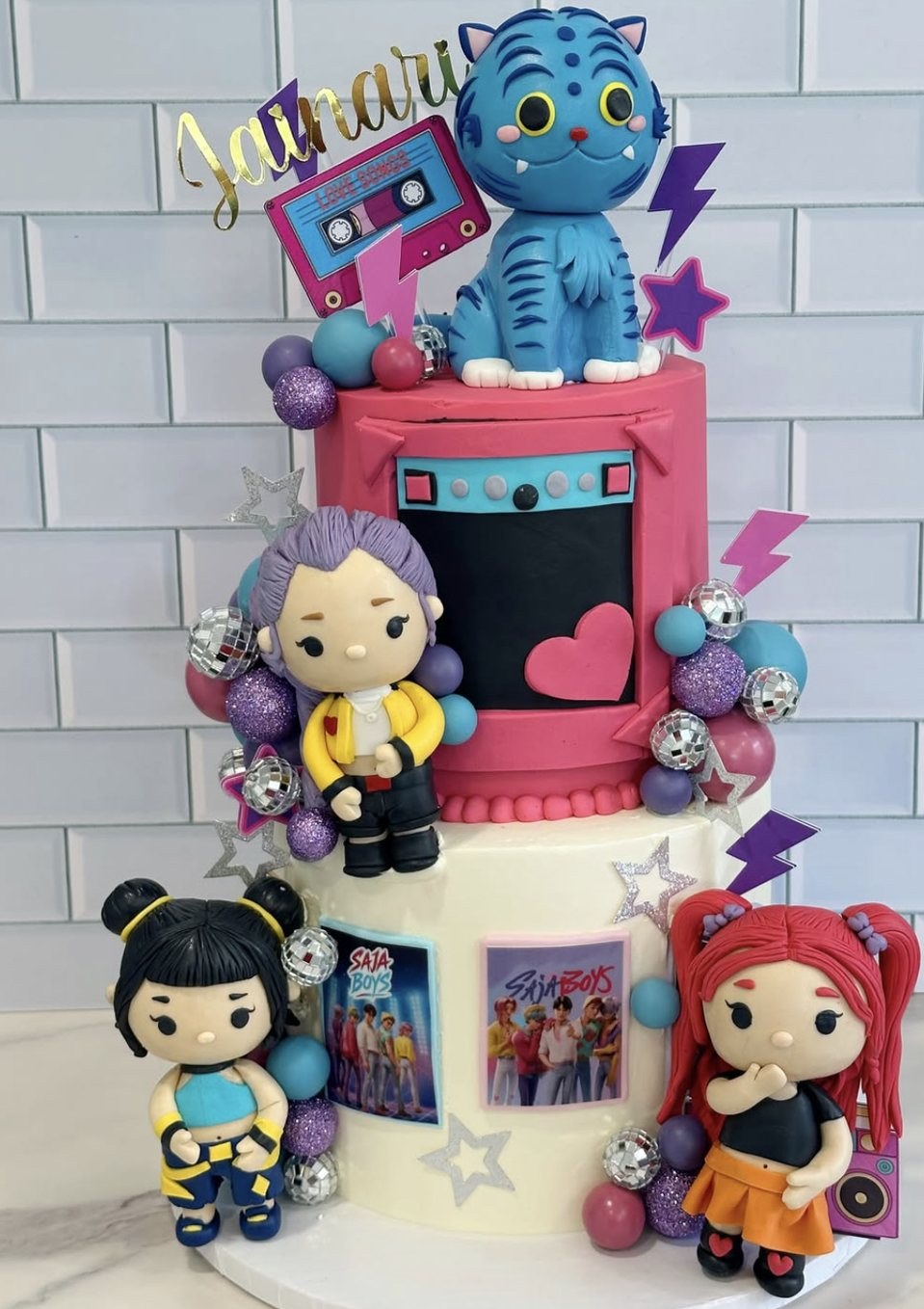 Pink and cream two-tier K-pop themed cake with fondant character figures and disco balls