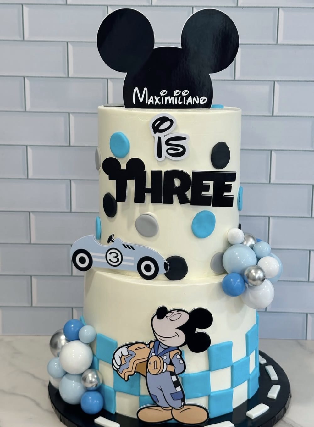 Cream and blue tiered Mickey Mouse racing themed cake for a 3rd birthday